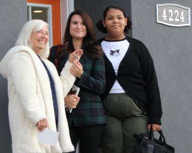 A woman hands a set of house keys to a mother and daughter.